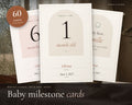 Baby Milestone Cards printable from Rooted & Refined: cover preview with the printed pages styled on a table