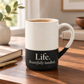 Life. Beautifully handled. engraved speckled mug in black on a sunlit wood table