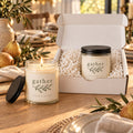 Gather olive sprig candle gift set: open gift box and a lit candle on a warm wood table