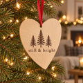 Wooden heart ornament with three evergreen trees and still & bright hanging on a lit Christmas tree
