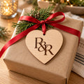 Wooden heart ornament with an R&R monogram tied with red ribbon to a kraft-wrapped gift with pine
