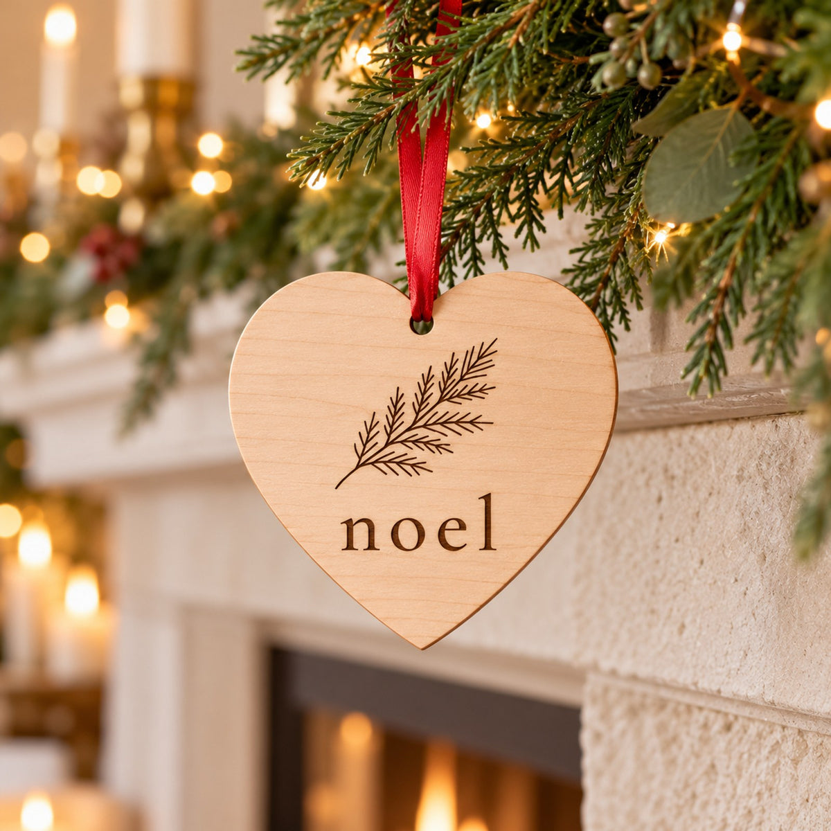 Wooden heart ornament with a pine branch and noel hanging from garland on a mantel with candles