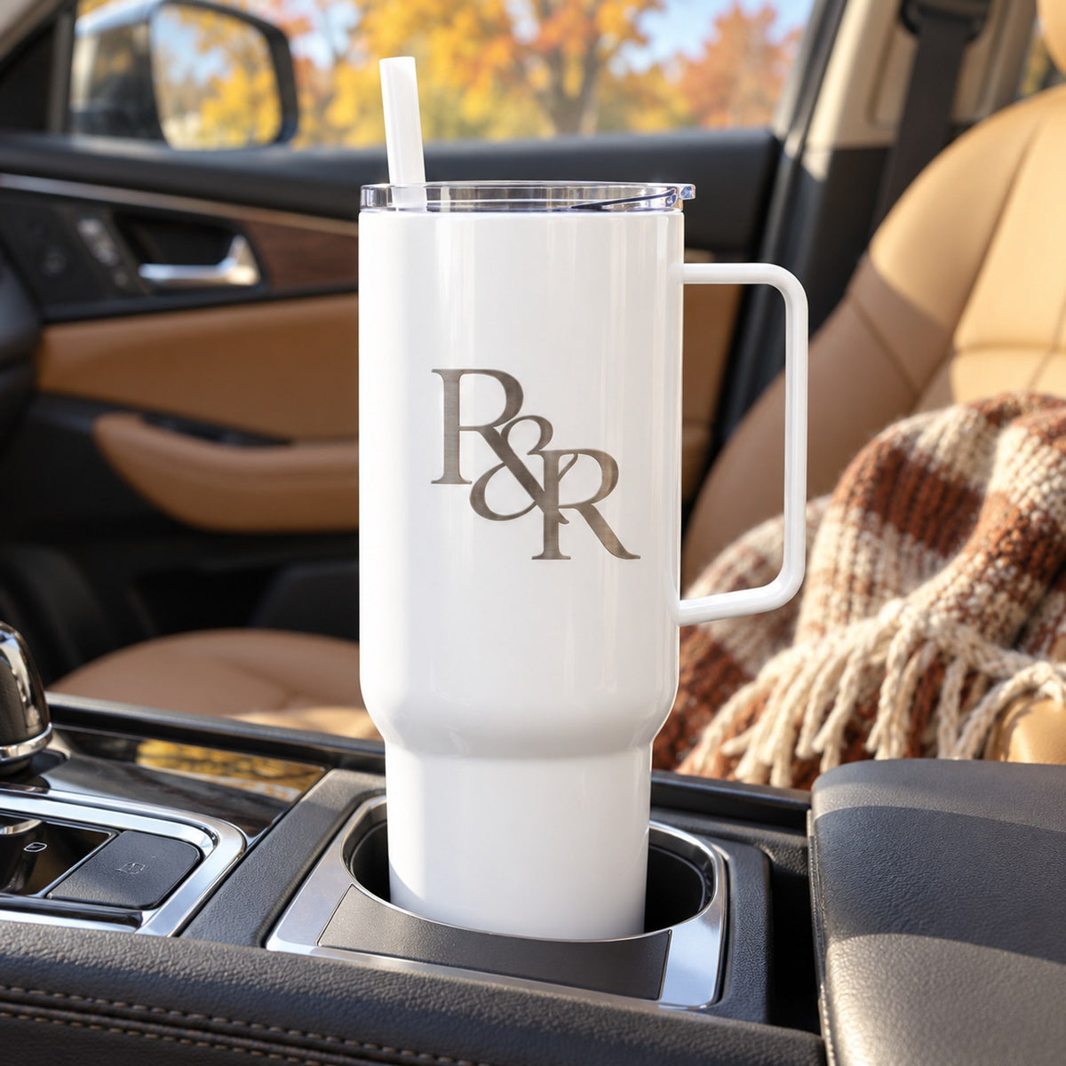 White 40 oz tumbler with handle engraved with an R&R monogram in a car cup holder with a plaid scarf