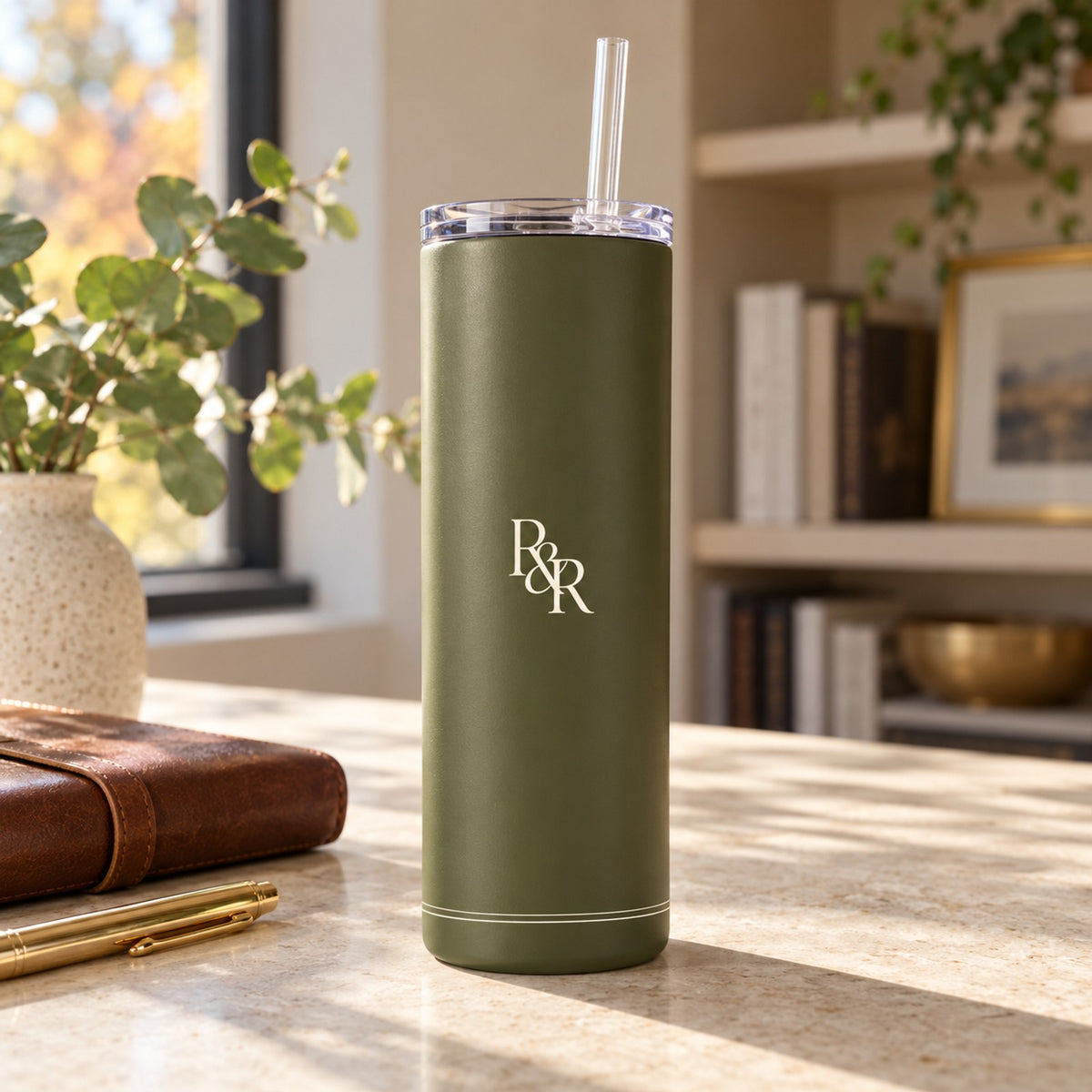 Moss green tumbler with a cream R&R monogram on a stone counter with a leather journal and eucalyptus