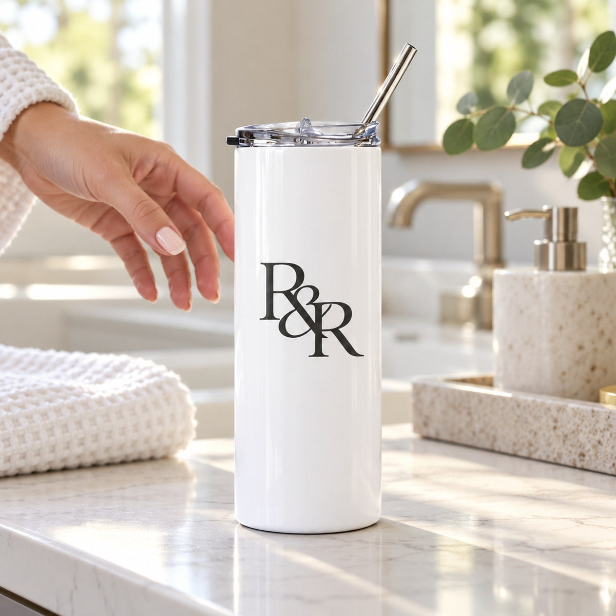White skinny tumbler with a black R&R monogram on a marble bathroom counter with a folded towel