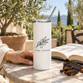 White skinny tumbler with an olive branch and stay rooted on a stone patio table with a book and sunglasses