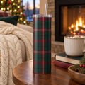 Bordeaux and pine tartan tumbler on a side table by a lit fireplace with cocoa, books and a knit throw