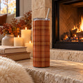 Rust and gold tartan 20 oz tumbler on a stone hearth by a lit fireplace with candles and books