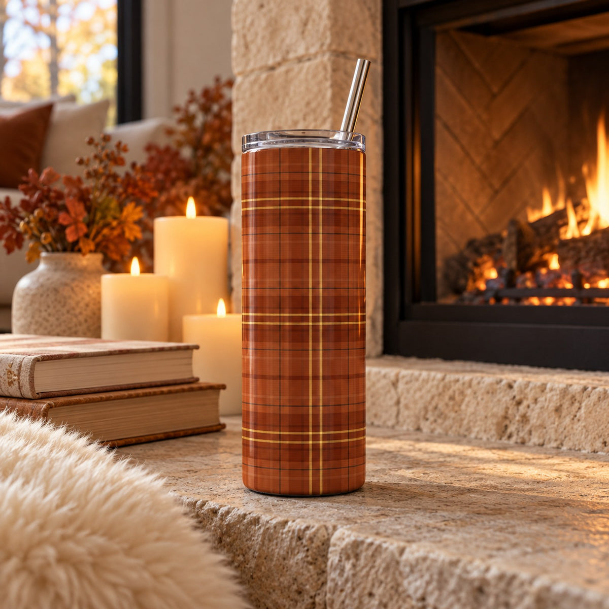 Rust and gold tartan 20 oz tumbler on a stone hearth by a lit fireplace with candles and books