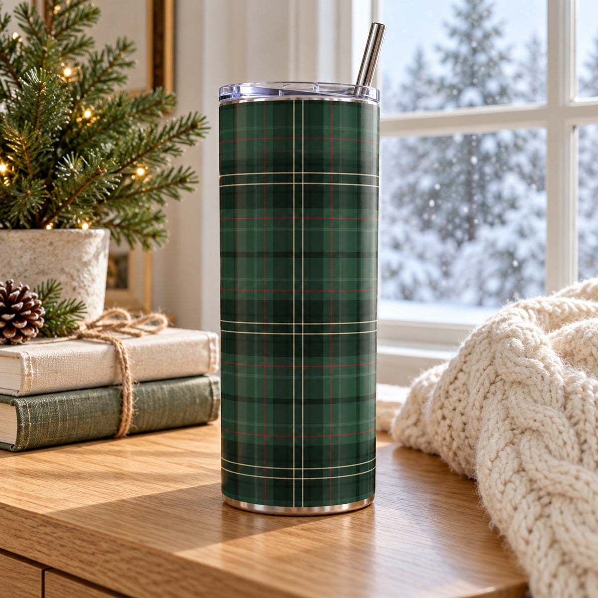 Forest green tartan 20 oz tumbler with straw on a wooden table by a snowy window, pine and wrapped books