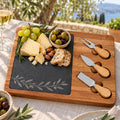 Acacia and slate charcuterie board engraved with an olive branch, with cheese, grapes and olives on a sunny terrace