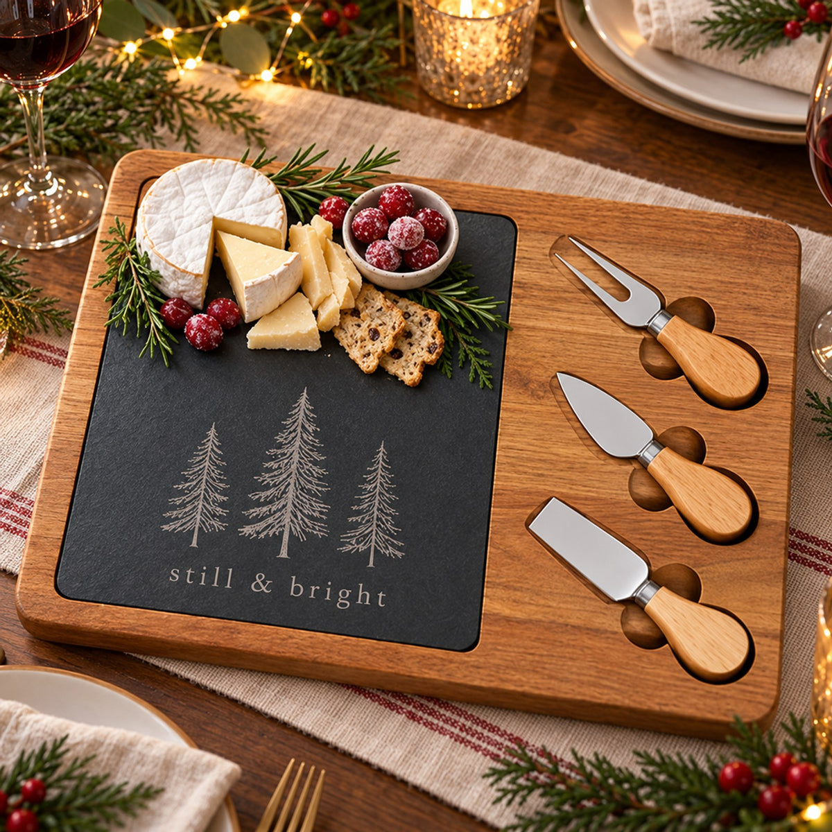 Acacia and slate charcuterie board engraved with evergreens and still & bright on a Christmas dinner table