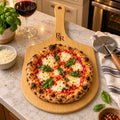 Bamboo pizza board engraved with an R&R monogram, with a margherita pizza and basil on a kitchen counter