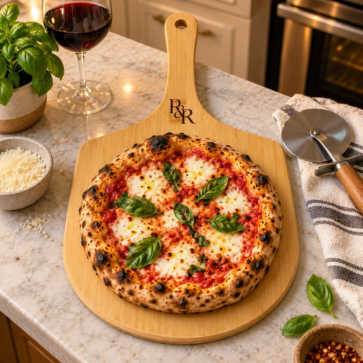 Bamboo pizza board engraved with an R&R monogram, with a margherita pizza and basil on a kitchen counter
