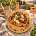 Bamboo pizza board engraved with a swag of olive branches, with burrata pizza on a terrace at golden hour