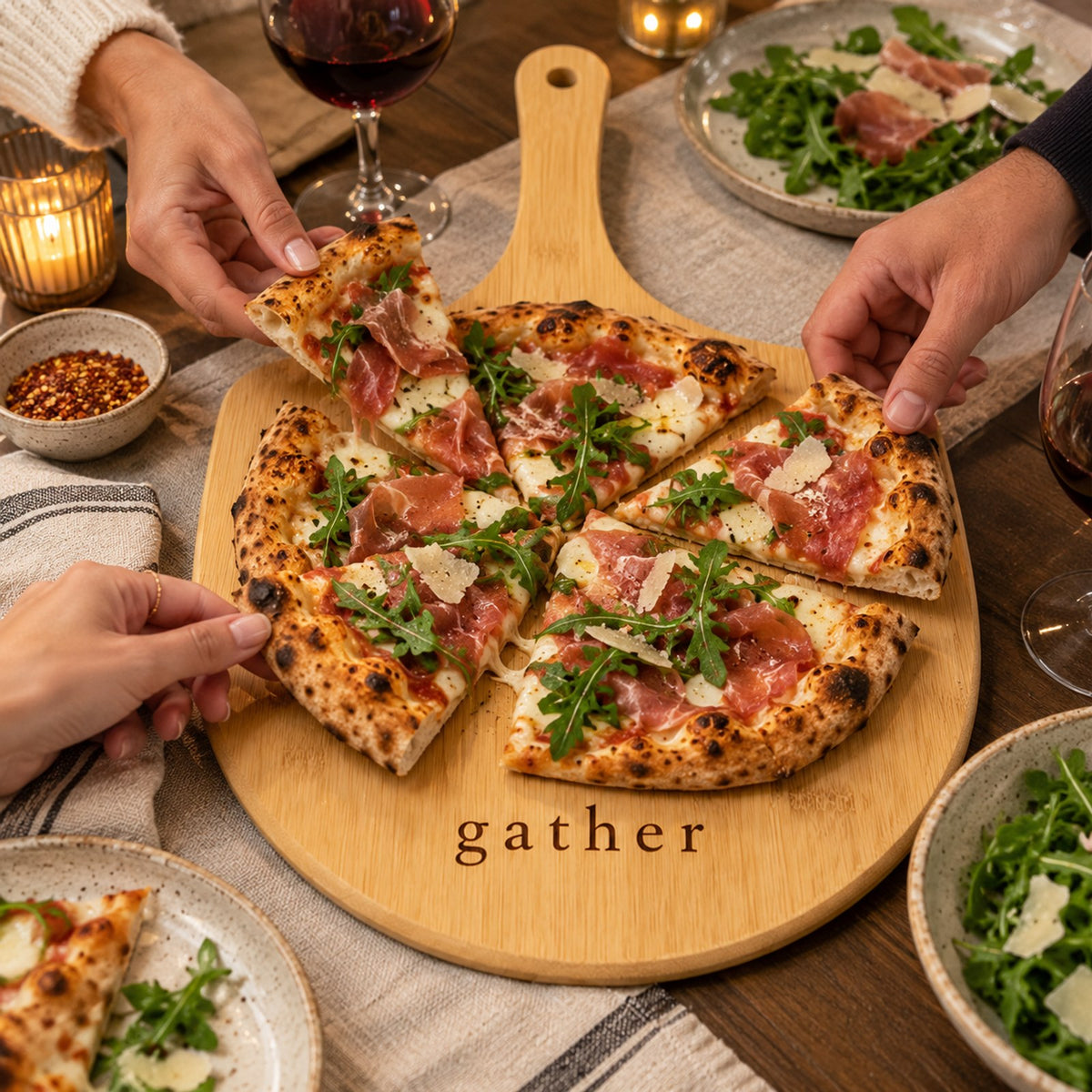 Bamboo pizza board engraved with gather, with friends sharing a prosciutto and arugula pizza