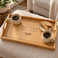 Bamboo serving tray engraved with the Rooted & Refined name and an olive sprig, with two coffees and biscotti