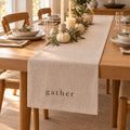 Oatmeal table runner printed with gather on a Thanksgiving table with white pumpkins, olive branches and candles