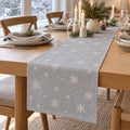 Slate blue table runner with white snowflakes on a winter table by a snowy window with pine and candles