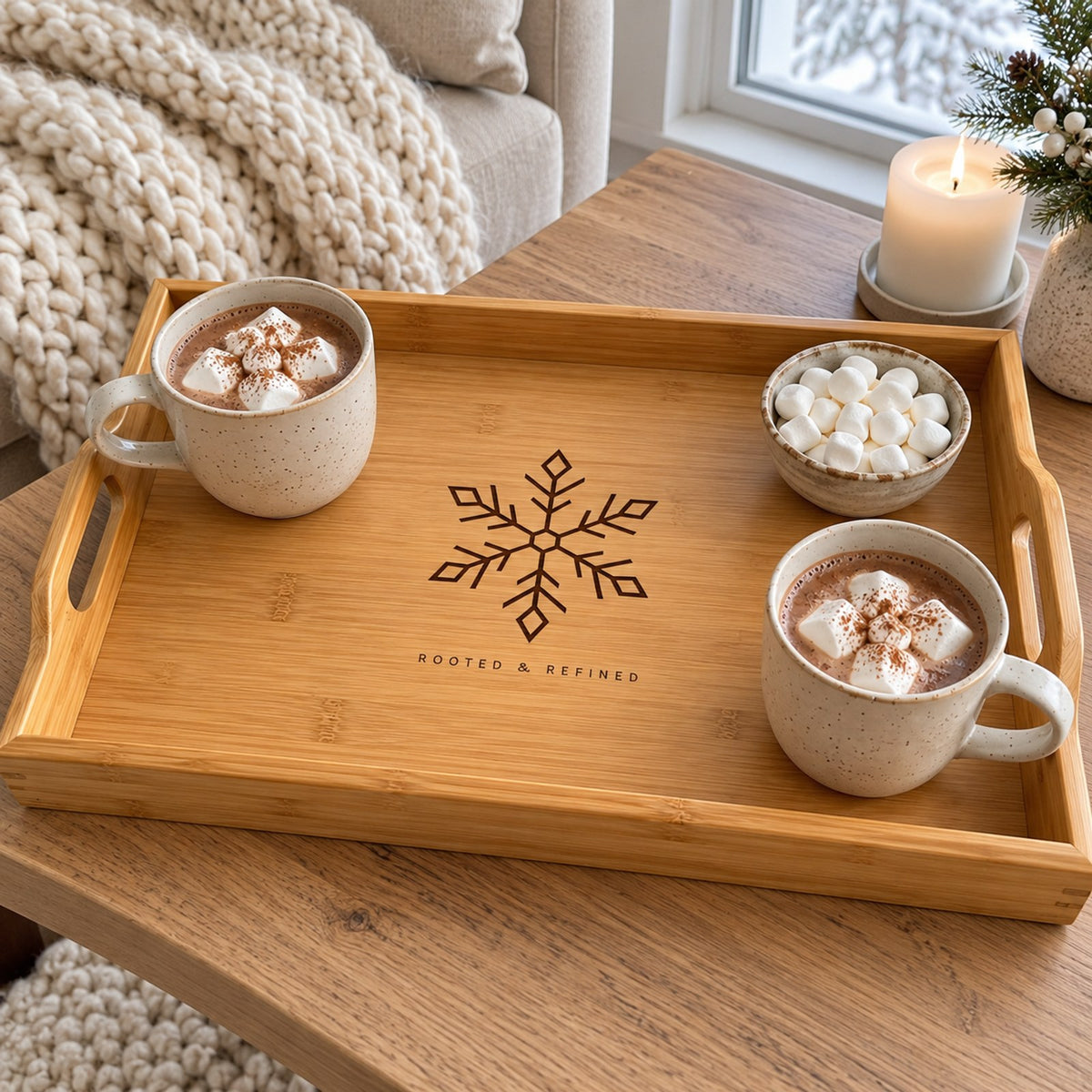 Bamboo serving tray engraved with a snowflake, with mugs of cocoa and marshmallows by a snowy window