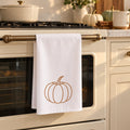 White tea towel with a line-drawn pumpkin hanging on a cream oven door in a fall kitchen
