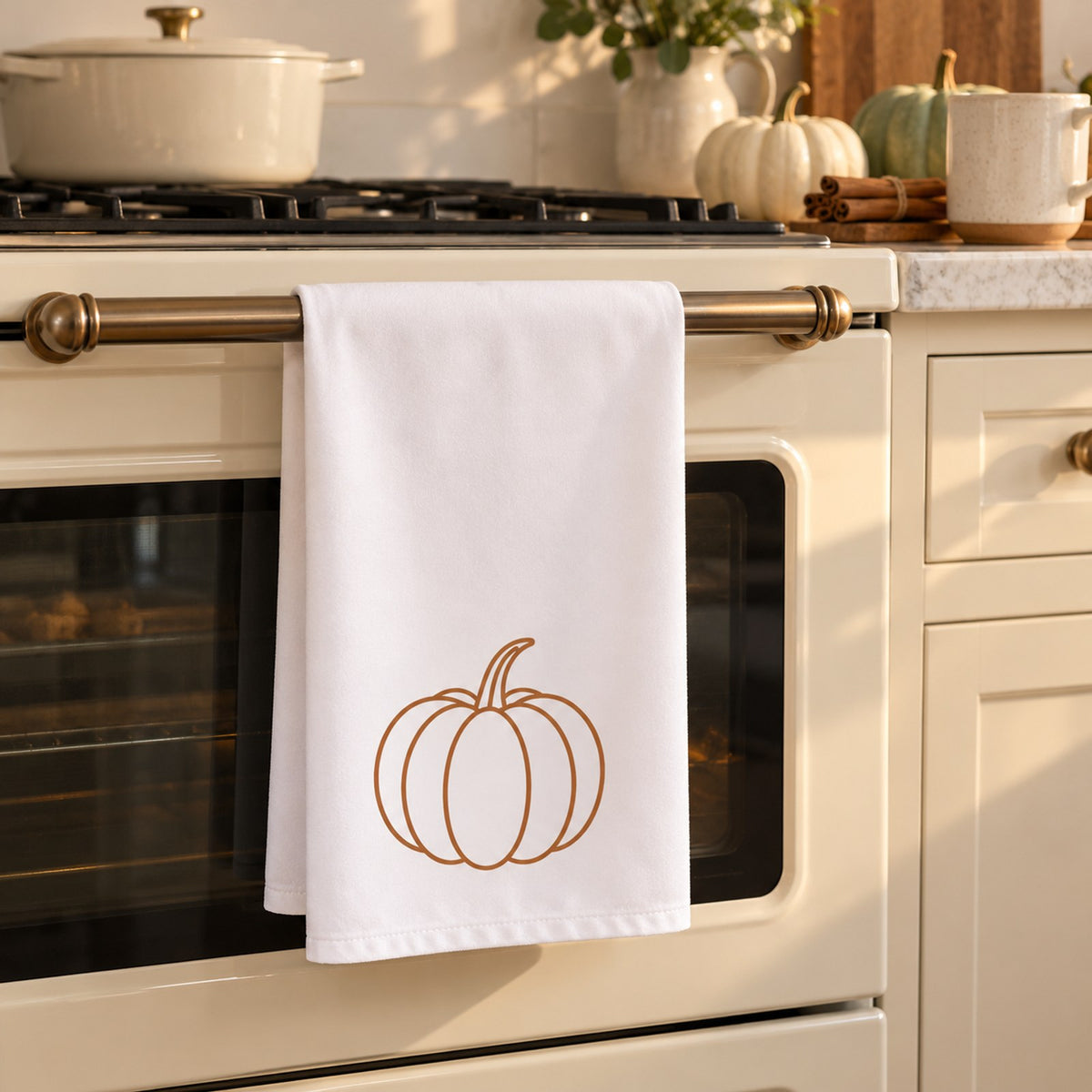 White tea towel with a line-drawn pumpkin hanging on a cream oven door in a fall kitchen
