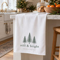 White tea towel with three evergreen trees and still & bright on a kitchen island at Christmas