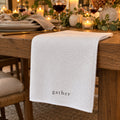 White waffle tea towel printed with gather draped on a wooden table set for a candlelit dinner