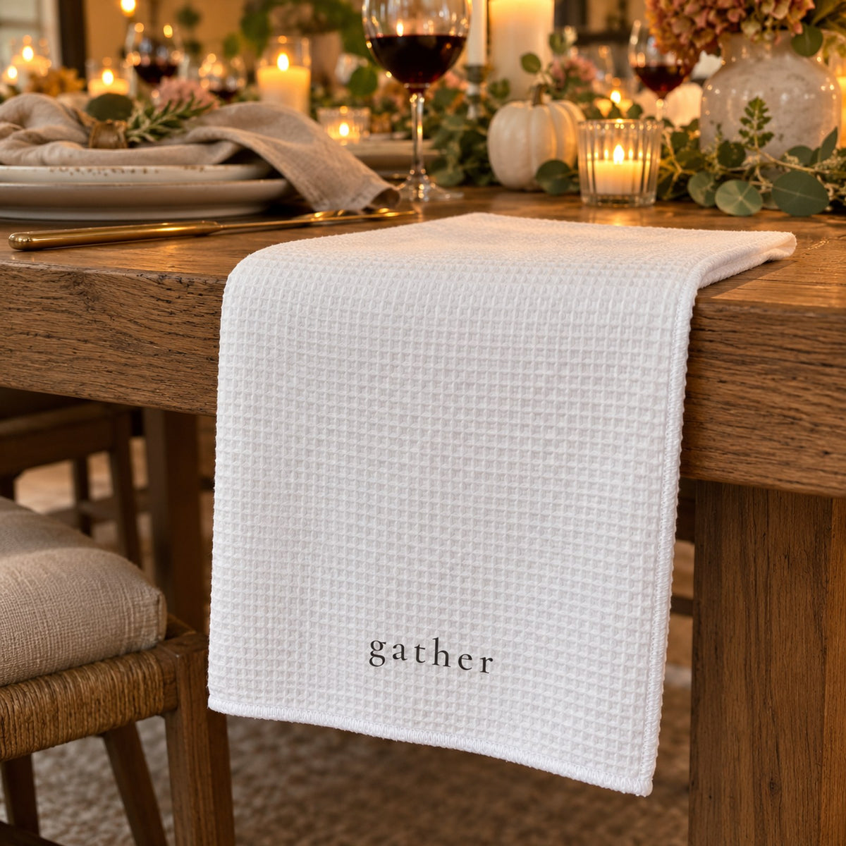 White waffle tea towel printed with gather draped on a wooden table set for a candlelit dinner