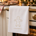 White waffle tea towel with a gold gingerbread man hanging on an oven beside gingerbread cookies