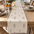 Linen table runner with red winter berries and sage sprigs on a holiday table with clementines and pine