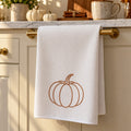 White waffle tea towel with a line-drawn pumpkin hanging on a brass oven rail in a fall kitchen