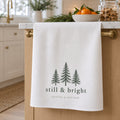 White waffle tea towel with evergreen trees and still & bright hanging on a kitchen island at Christmas