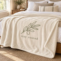Ivory sherpa fleece blanket with an olive branch and stay rooted in soft charcoal, draped over a linen bed