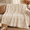 Ivory sherpa fleece blanket with an all-over small camel pumpkin pattern, draped over a cream sofa