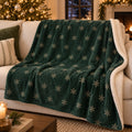 Forest green sherpa fleece blanket with an all-over ivory snowflake pattern, on a sofa by a lit Christmas tree and fireplace