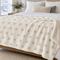 Ivory sherpa fleece blanket with an all-over grey snowflake pattern, across a bed by a snowy window