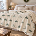 Ivory sherpa fleece blanket with an all-over green evergreen tree pattern, across a neutral bed