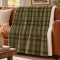Olive green tartan sherpa fleece blanket with gold lines, draped over a cognac leather sofa
