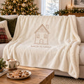 Ivory sherpa fleece blanket with a line-drawn gingerbread house and home for the holidays, on a sofa with cocoa and cookies