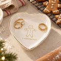 Gold-rimmed white heart trinket dish with a gilded gingerbread man, holding gold rings beside gingerbread cookies
