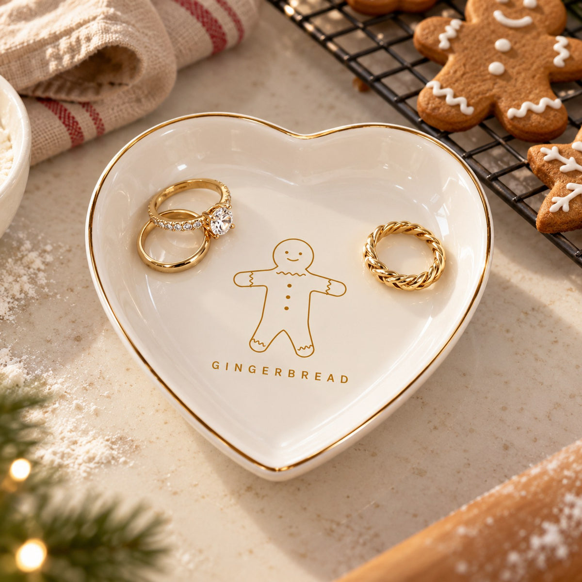 Gold-rimmed white heart trinket dish with a gilded gingerbread man, holding gold rings beside gingerbread cookies
