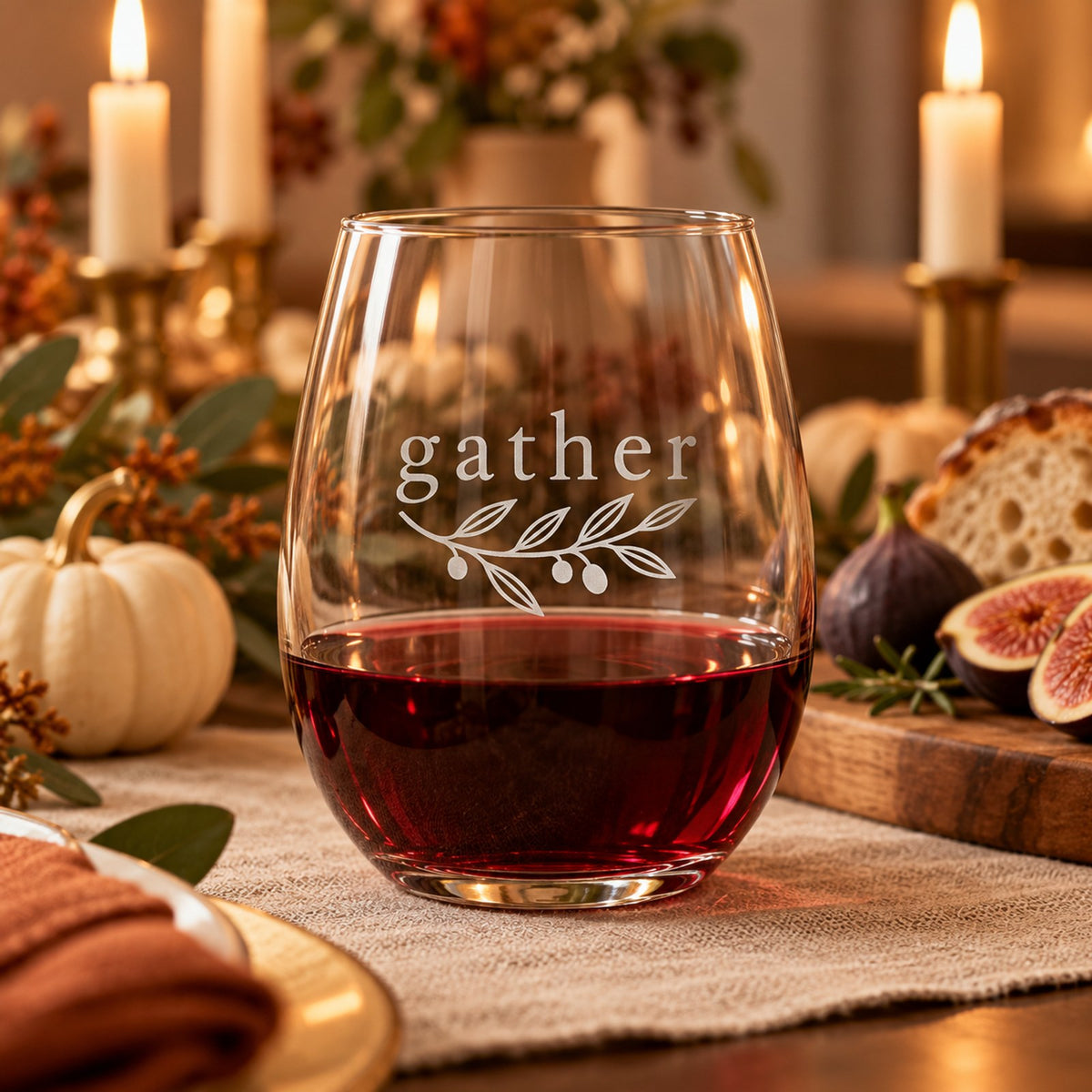 Stemless wine glass etched with gather and an olive sprig, with red wine on a candlelit fall table with figs