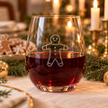 Stemless wine glass etched with a gingerbread man, with red wine beside gingerbread cookies and candles