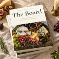 The Board: Charcuterie, Graze Boxes & Food Boards hardcover cookbook by Rachelle Merchant, two copies stacked on linen