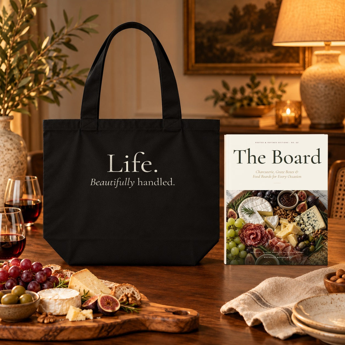 The Board Cookbook & Tote Set: The Board paperback cookbook by Rachelle Merchant beside the black Life. Beautifully Handled. Organic Cotton Tote with a charcuterie spread