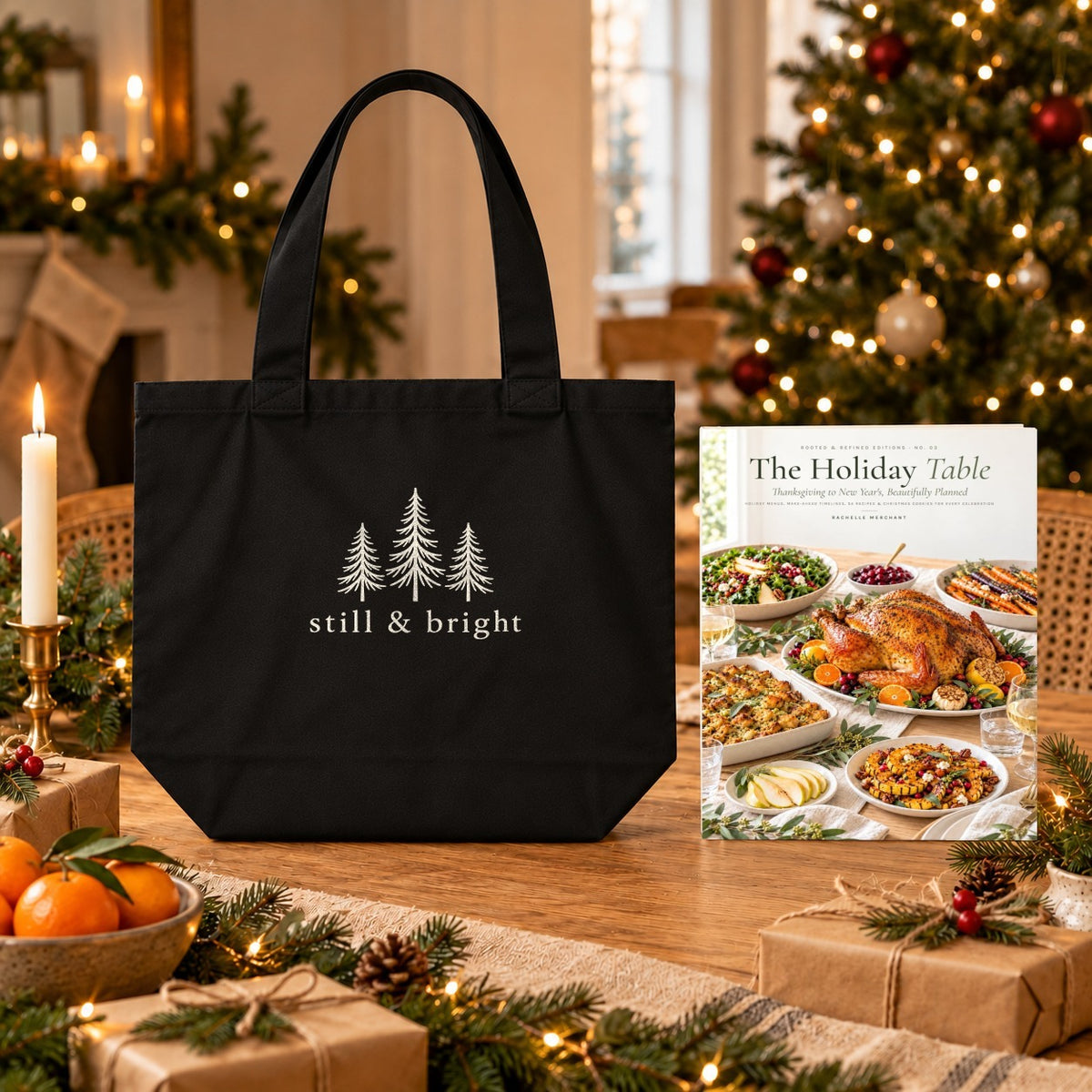 The Holiday Table Cookbook & Tote Set: The Holiday Table paperback cookbook by Rachelle Merchant beside the black Still & Bright Evergreen Organic Cotton Tote on a Christmas table