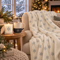 Snowflake Cozy Night In Gift Set by Rooted & Refined: matching sherpa throw draped on a chair with the lit frosted candle and engraved mug beside it