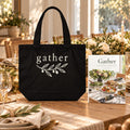 Gather Cookbook & Tote Set: the Gather paperback cookbook by Rachelle Merchant beside the black Gather Shoulder Tote on a dining table set for guests