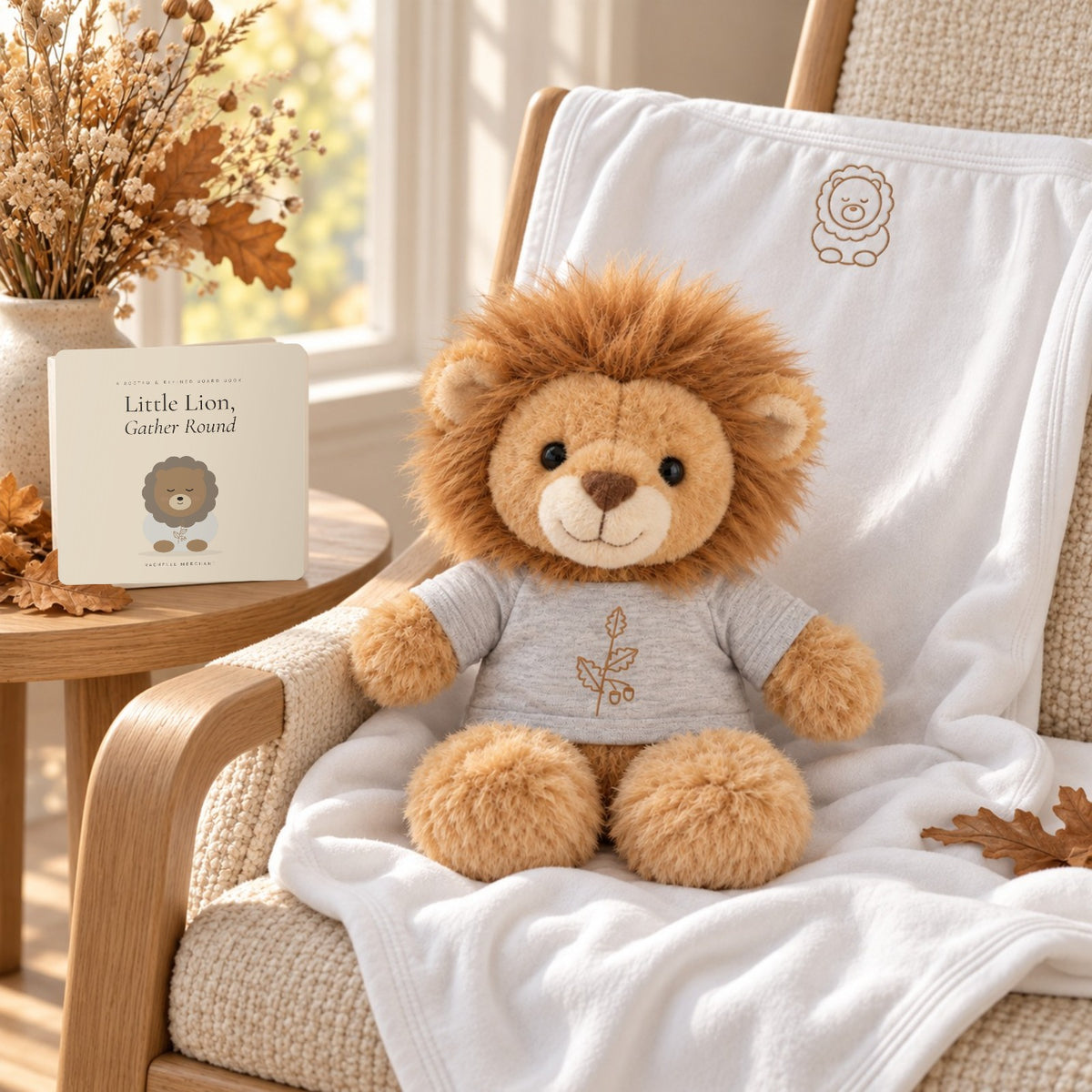 Little Lion Book, Plush & Blanket Gift Set by Rooted & Refined: the Little Lion plush on the white embroidered jersey blanket draped over a nursery rocking chair, with the Little Lion, Gather Round board book
